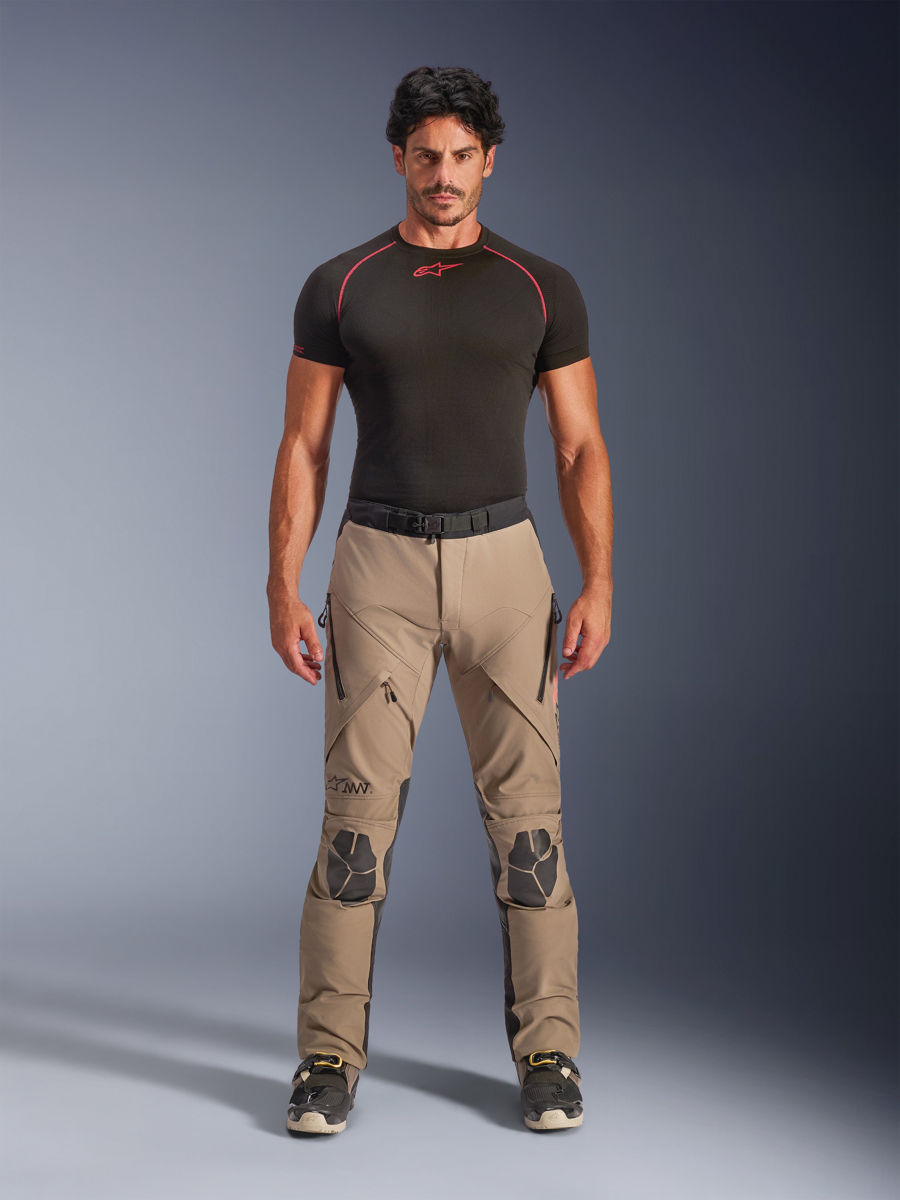 Manlig modell i Alpinestars AMT-8 Stretch Drystar® XF byxor i Walnut och Black, kombinerat med ett svart kortärmat baslager, äventyrsbyxor för touring med förstärkta knän, dragkedjeförsedd ventilation och ergonomisk stretchdesign.