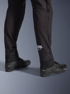 Alpinestars Aeroshell Pants, Black softshell motorcycle pants, close-up of lower leg and elasticated hem, white Alpinestars logo on calf, styled with black riding shoes, modern crossover sport design
