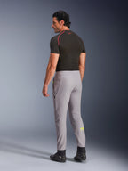 Alpinestars Aeroshell-byxor, Mid Gray Yellow Fluo, baksidesvy av manlig modell i stretchiga softshell-motorcykelbyxor, gul Astars-logotyp på vänster vad, matchade med ett svart baslager och körskor för en modern sportig silhuett.