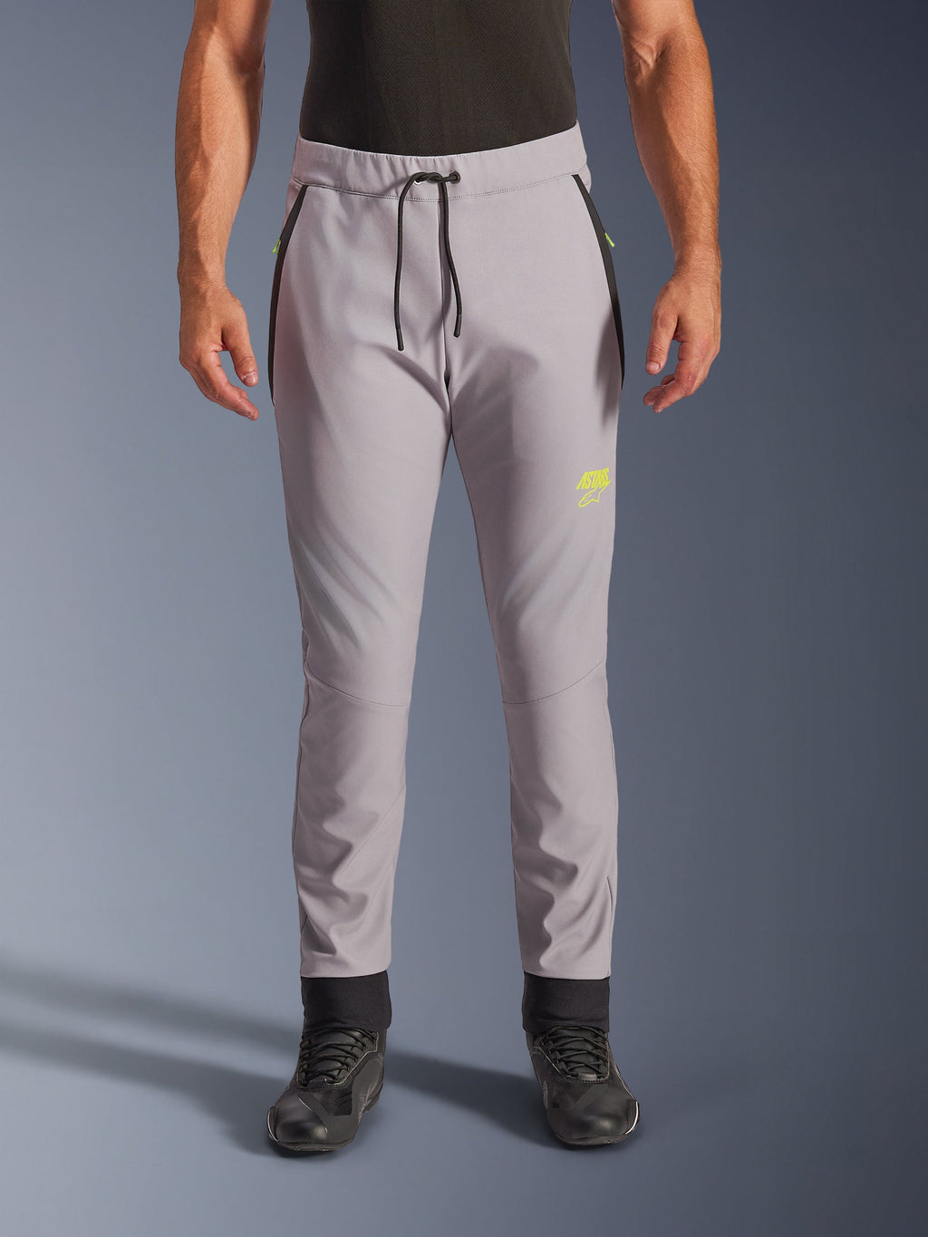 Alpinestars Aeroshell Pants, mellangrå och neongula, crossover softshell-motorcykelbyxor med svart dragsko i midjan och åtsittande benslut, gul logotyp på vänster lår, förböjda knän, sportig jogger-silhuett