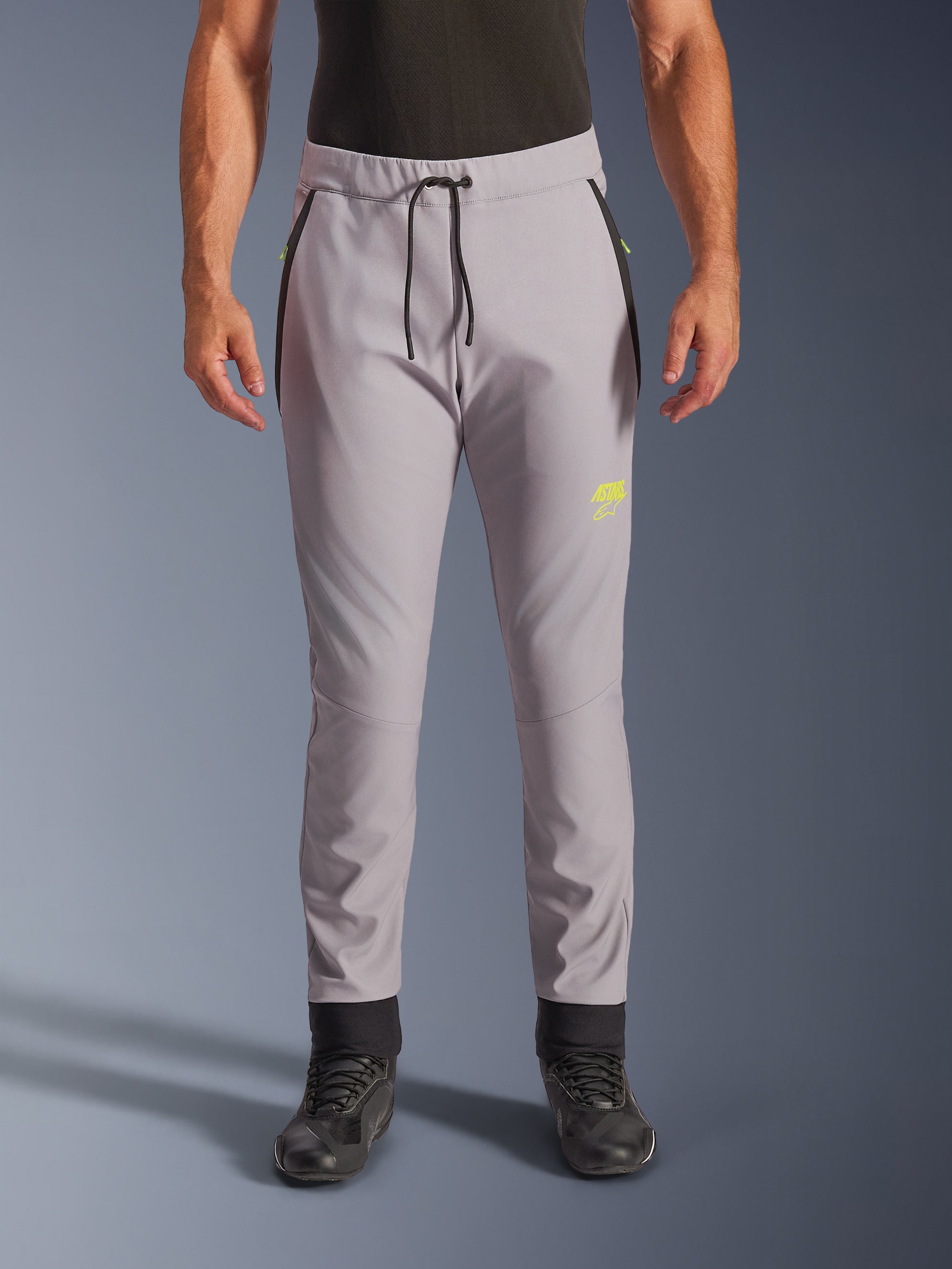 Alpinestars Aeroshell Pants, mellangrå och neongula, crossover softshell-motorcykelbyxor med svart dragsko i midjan och åtsittande benslut, gul logotyp på vänster lår, förböjda knän, sportig jogger-silhuett