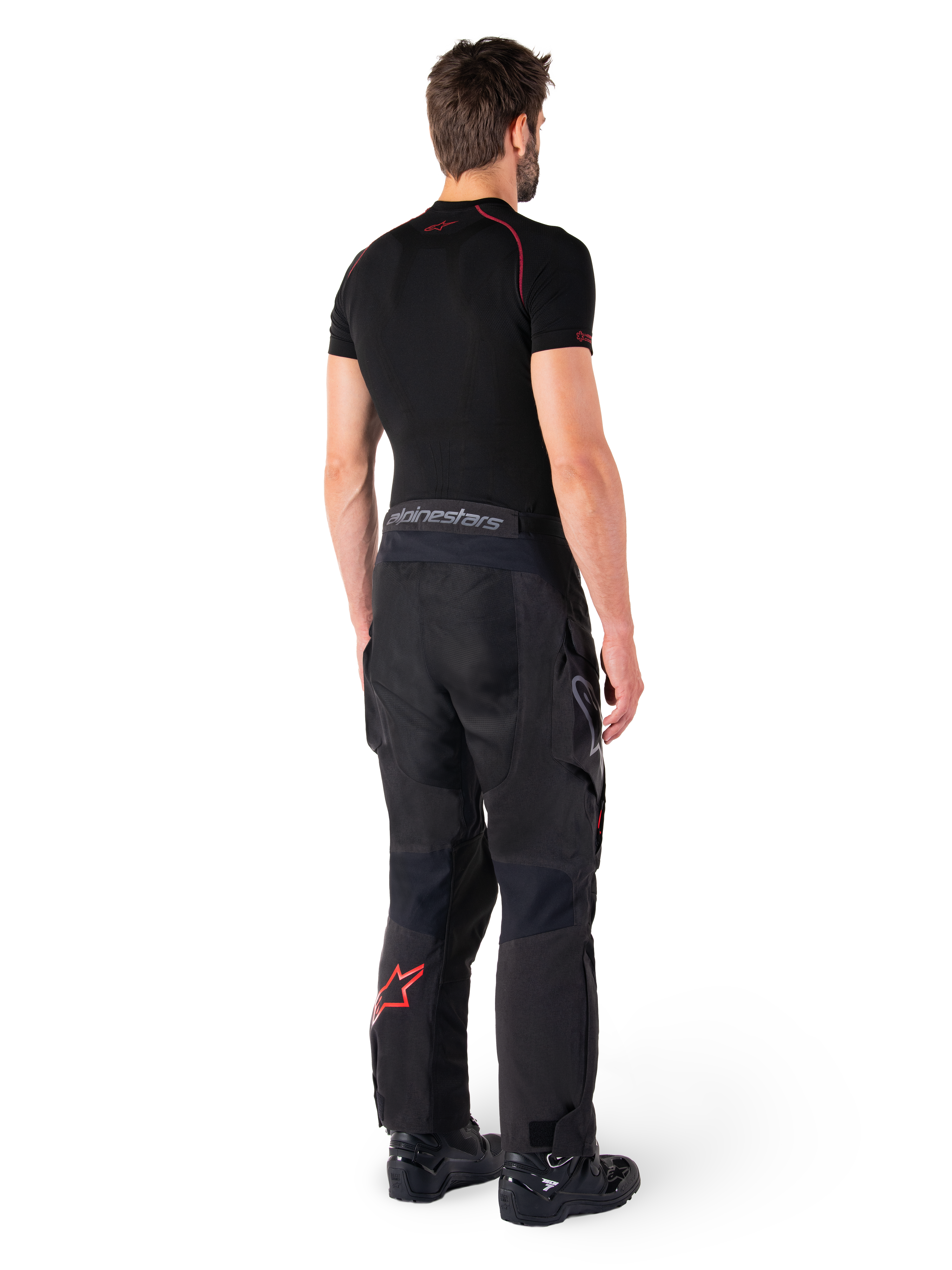 Alpinestars Hyde XT Drystar® Pants, Adventure Touring Pants, Black and Bright Red, rear view of a rider wearing the pants with a black base layer and black boots, featuring durable textile construction with a red star logo on the lower leg and gray Alpinestars branding on the waistband