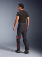Alpinestars Halo Pro Drystar® XF laminerade byxor, Black Dark Shadow med röda detaljer, bakifrån på manlig modell, kombinerade med ett svart underställ och motorcykelstövlar, teknisk adventure-touringutrustning för terrängkörning