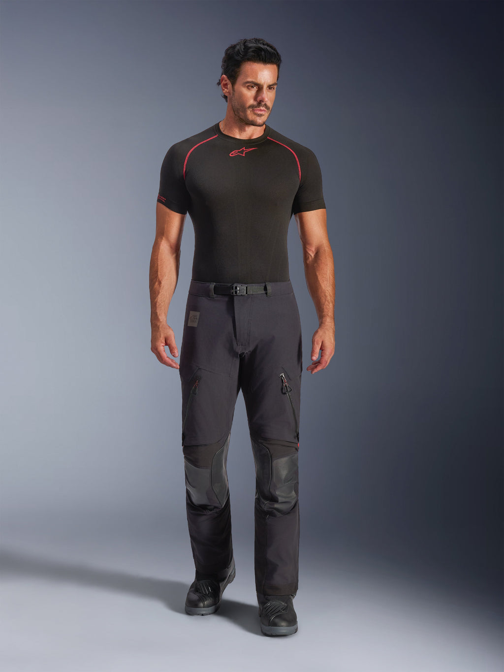 Alpinestars Halo Pro Drystar® XF laminerade byxor i Black Dark Shadow, bärs av en modell med svart underställ och motorcykelstövlar, med tekniska lårventiler med dragkedja, benfickor och förstärkta knäpaneler, adventure touring-motorcykelutrustning.