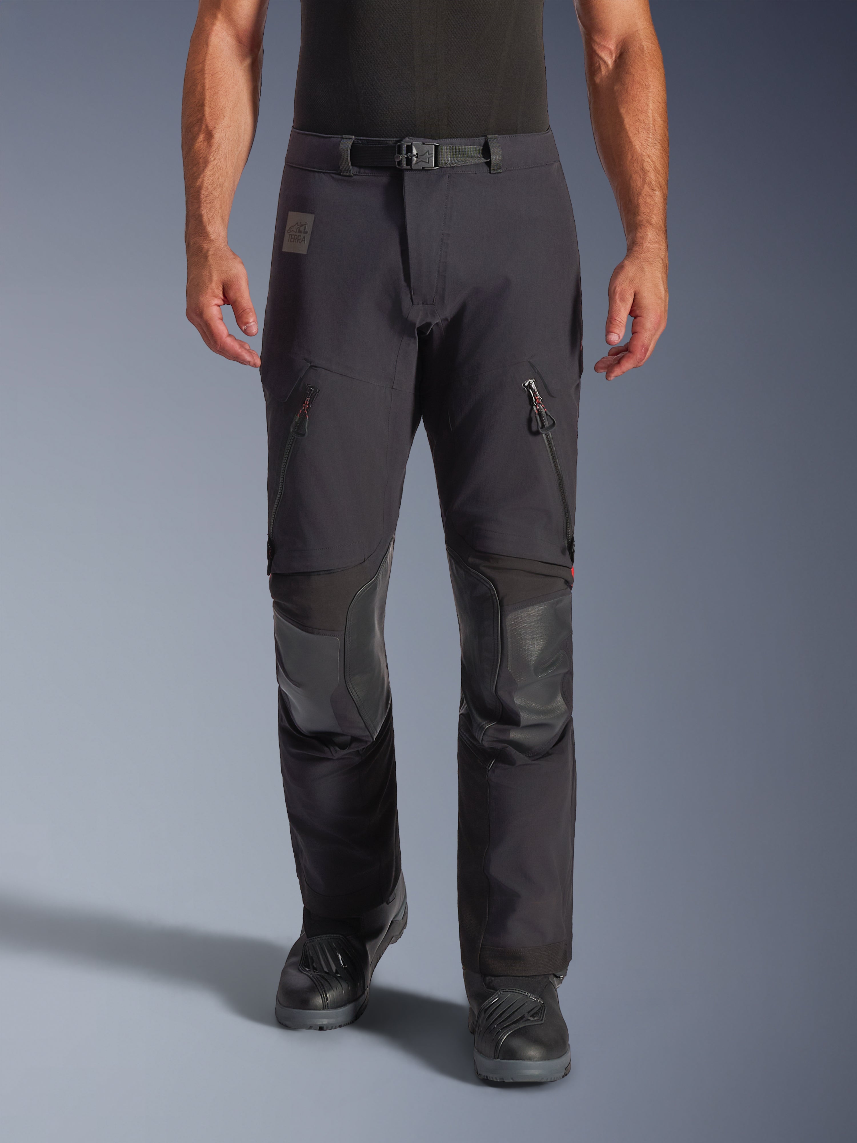 Alpinestars Halo Pro Drystar® XF Laminated Pants i Black Dark Shadow, äventyrsmotorcykelbyxor, frontvy på modell med magnetiskt midjespänne, ventilationsöppningar med dragkedja på låren och förstärkta knäpartier i läder, matchade med svarta MC-stövlar.