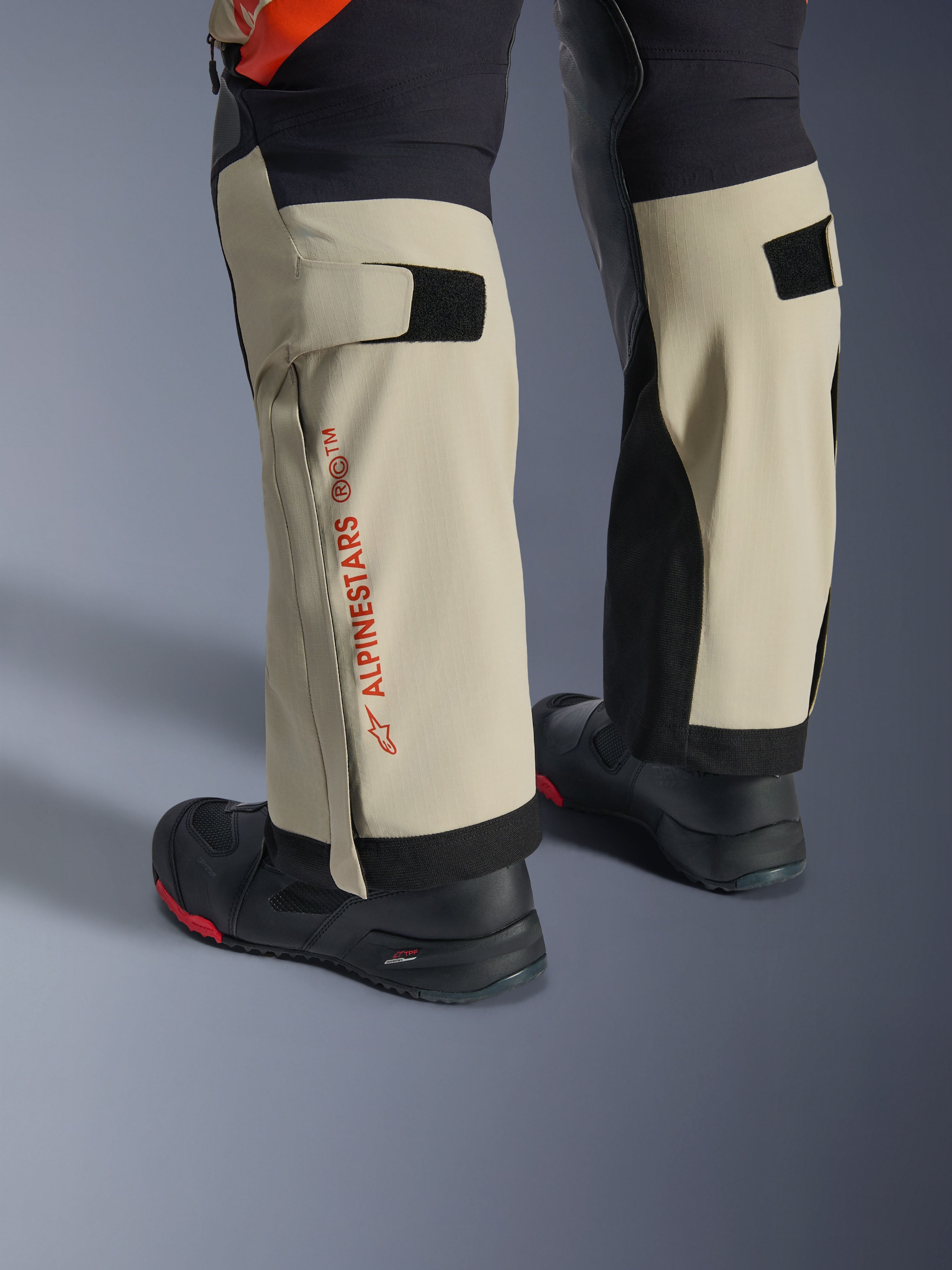 Alpinestars Halo Pro Drystar® XF laminerade byxor, Mastic Black, närbild på underbenen med röd Alpinestars-logotyp och kardborrejustering för vaderna, bärs med svarta äventyrsstövlar