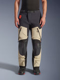 Alpinestars Halo Pro Drystar® XF laminerade byxor, äventyrsbyxor för motorcykel, Mastic Black, frontvy buren av en förare, med stora lårventiler med dragkedja, förstärkta svarta knäpaneler och beige textilkonstruktion, kombinerade med svarta och röda mc-stövlar.