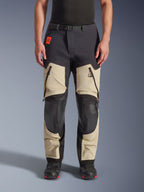 Alpinestars Halo Pro Drystar® XF laminerade byxor, äventyrsbyxor för motorcykel, Mastic Black, frontvy buren av en förare, med stora lårventiler med dragkedja, förstärkta svarta knäpaneler och beige textilkonstruktion, kombinerade med svarta och röda mc-stövlar.