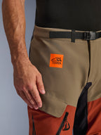 Alpinestars Halo Pro Drystar® XF laminerade byxor, Walnut Rust Black, närbild på det övre låret med ett ljusorange All Terra-logomärke, valnöts- och rostfärgade paneler och ett svart midjebälte med magnetspänne, äventyrsmotorcykelkläder