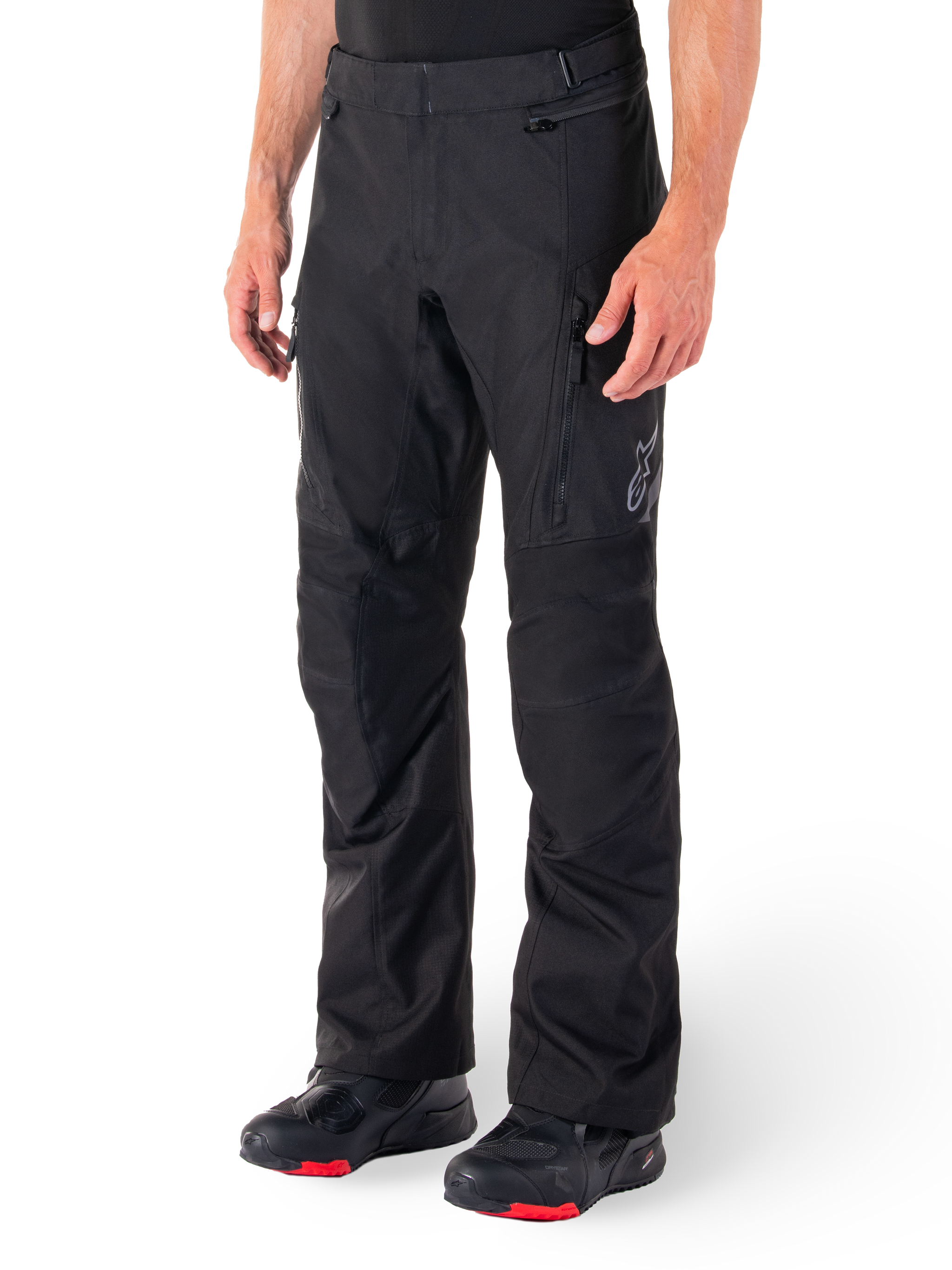 Alpinestars ST-1 Waterproof Pants, Black Motorcycle Touring Pants, worn with black and red riding boots, featuring zippered front pockets and a subtle star logo on the thigh, ergonomic design for adventure and road riding.