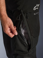Alpinestars Andes V4 Drystar Pants, Black, close-up of thigh ventilation vent being opened by a hand, mesh lining for airflow, waterproof zipper detail, featuring white Alpinestars logo branding