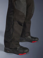 Alpinestars Andes V4 Drystar® Pants, Black adventure motorcycle pants, close-up of lower leg with side zipper detail, durable textile with ripstop reinforcements, worn with black boots featuring red soles