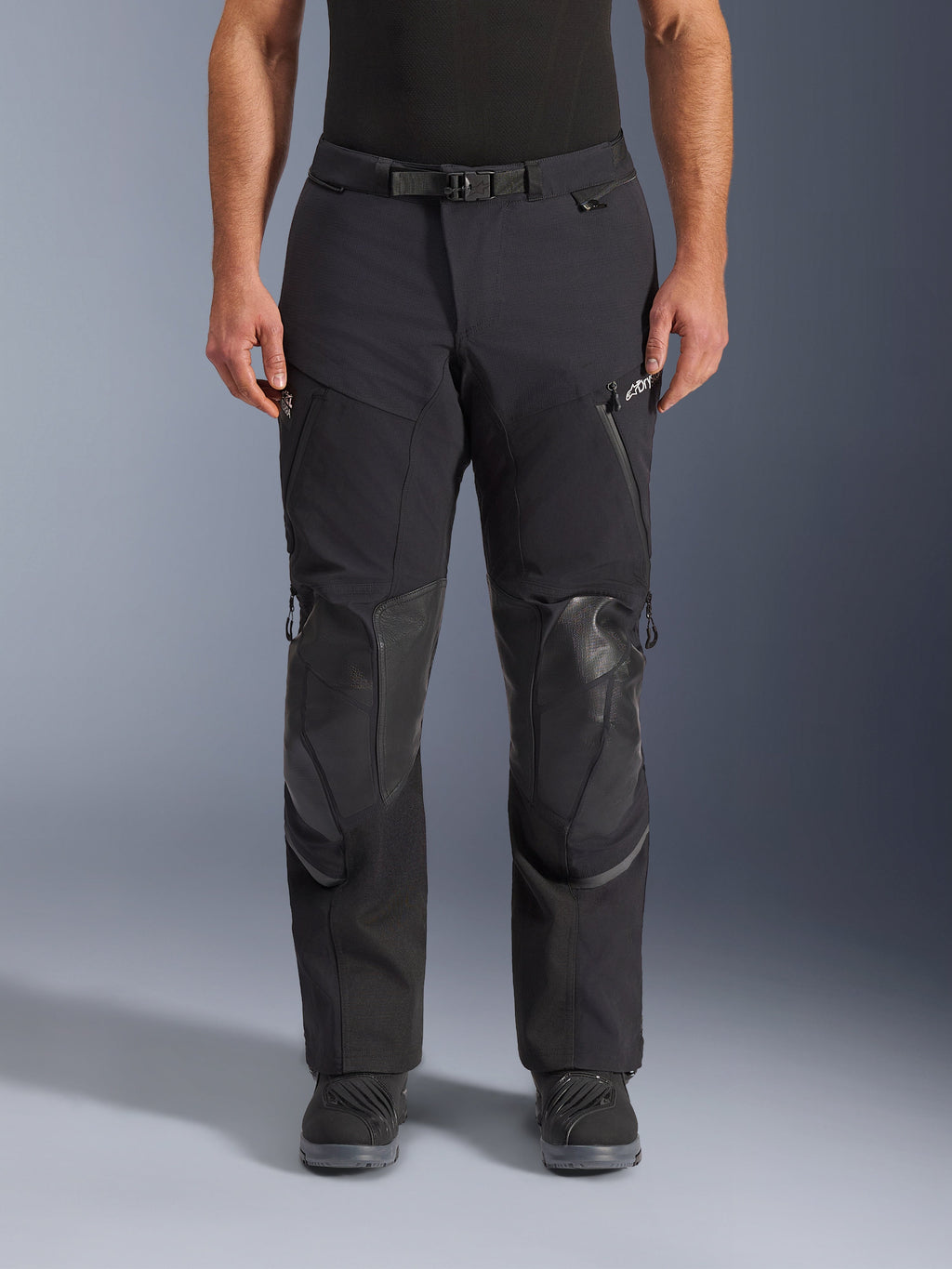 Alpinestars Andes Pro Drystar® XF byxor, svart mörkgrå adventure touring-motorcykelbyxor, framifrån, med 3-lagers laminerad konstruktion, integrerade knäskyddspaneler, vattentäta fickor med dragkedja och magnetiskt midjespänne, stylade med svarta MC-stövlar.