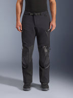 Alpinestars Andes Pro Drystar® XF byxor, svart mörkgrå adventure touring-motorcykelbyxor, framifrån, med 3-lagers laminerad konstruktion, integrerade knäskyddspaneler, vattentäta fickor med dragkedja och magnetiskt midjespänne, stylade med svarta MC-stövlar.