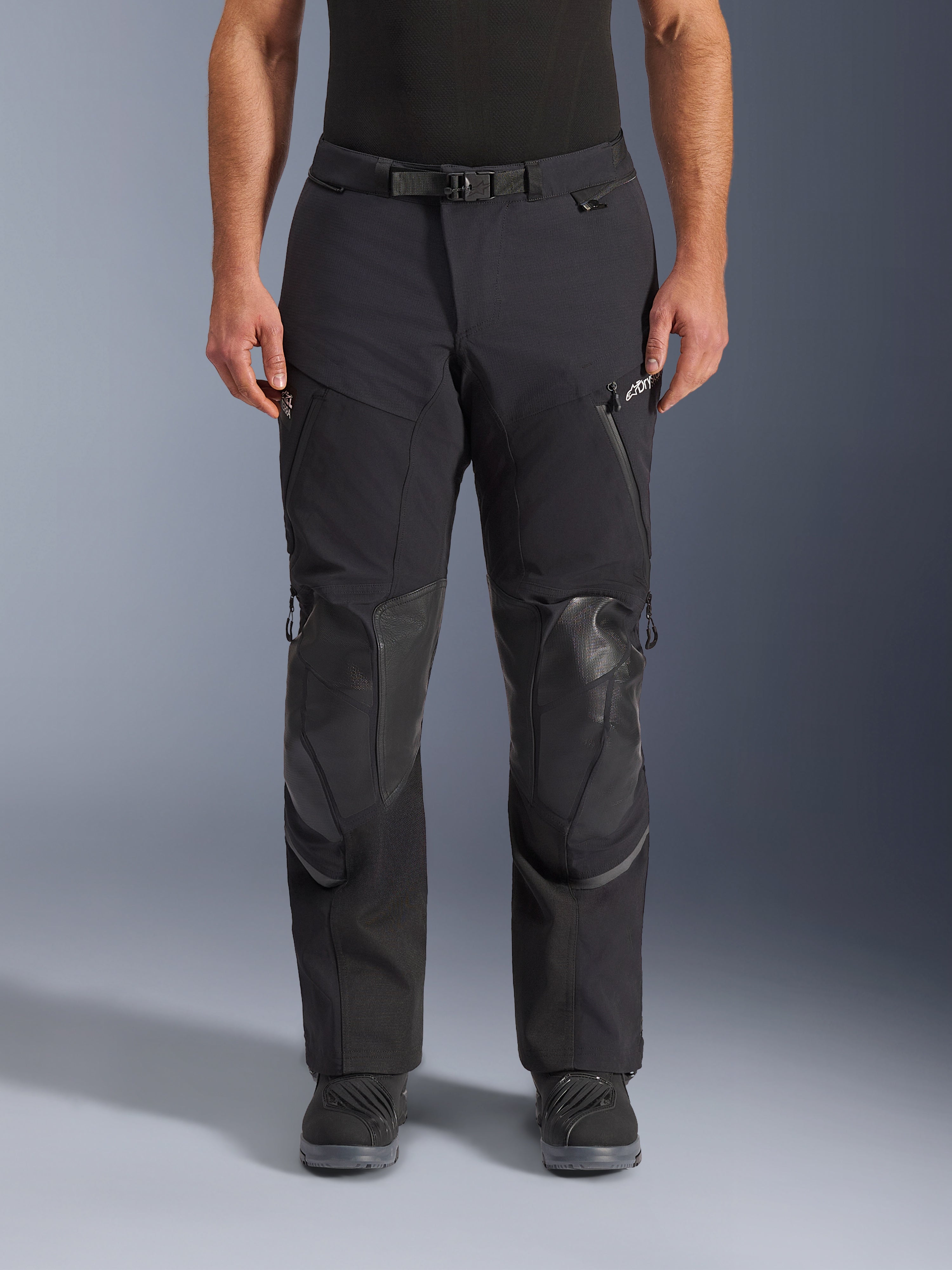 Alpinestars Andes Pro Drystar® XF byxor, svart mörkgrå adventure touring-motorcykelbyxor, framifrån, med 3-lagers laminerad konstruktion, integrerade knäskyddspaneler, vattentäta fickor med dragkedja och magnetiskt midjespänne, stylade med svarta MC-stövlar.