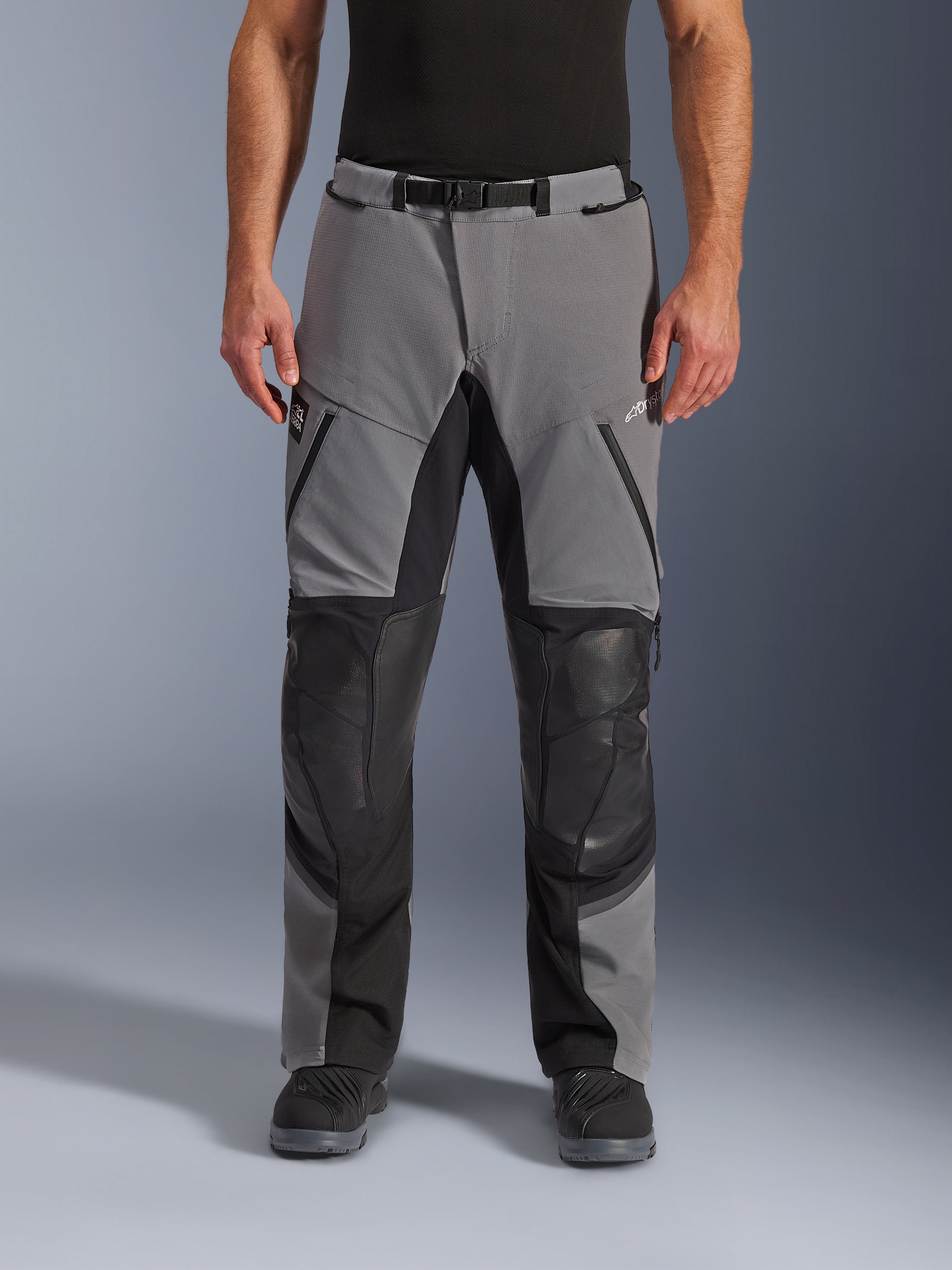 Alpinestars Andes Pro Drystar® XF byxor, motorcykelbyxor, mörkgrå och svarta, vy framifrån, med förstärkta svarta knäpaneler, vattentäta dragkedjor och bälte med magnetspänne, bärs med svarta stövlar