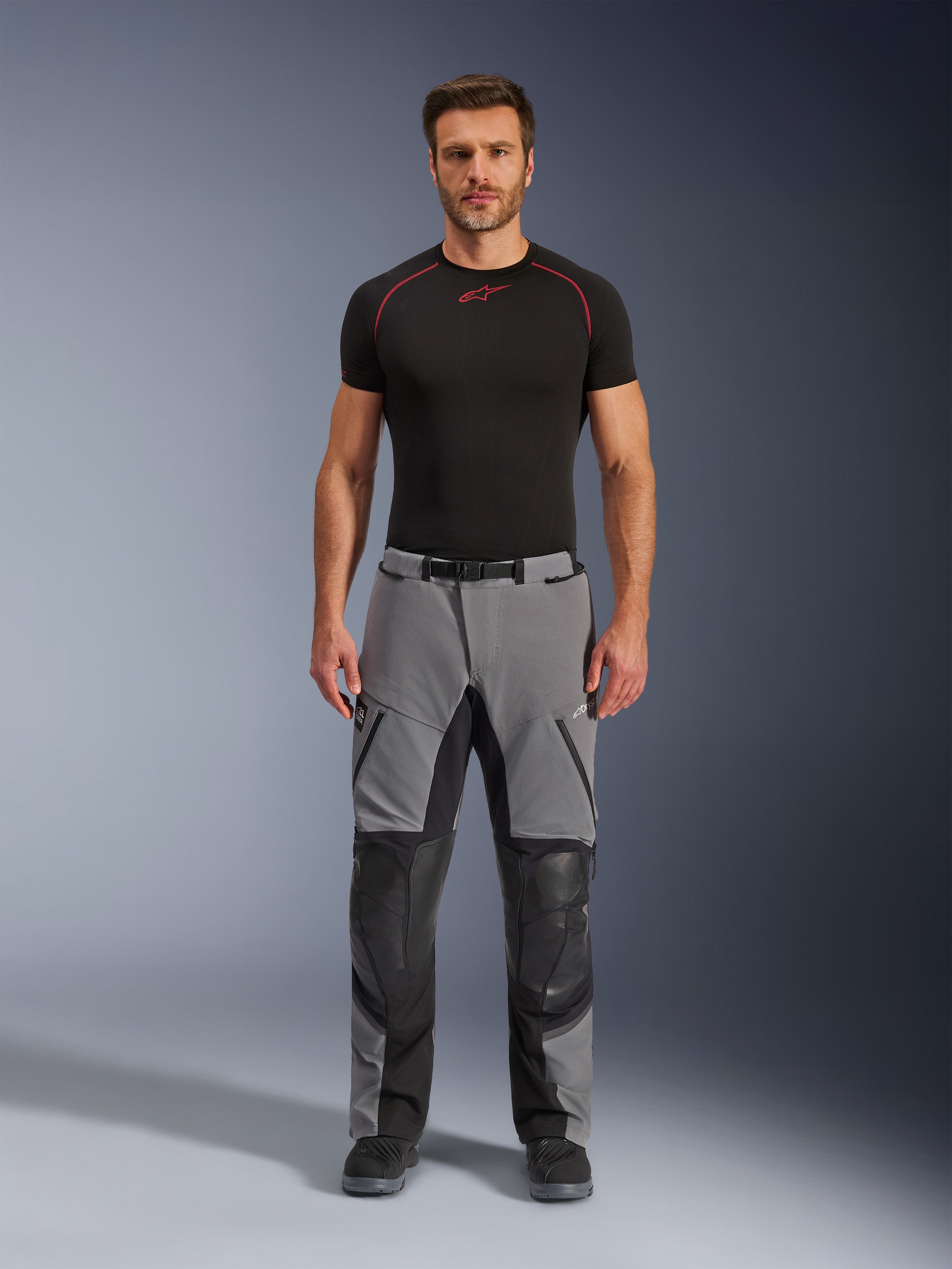 Alpinestars Andes Pro Drystar® XF-byxor, motorcykelbyxor för äventyrskörning, mörkgrå och svarta, framifrån på en modell med ett svart underställ, med förstärkta knäpaneler och vattentäta fickor med dragkedja