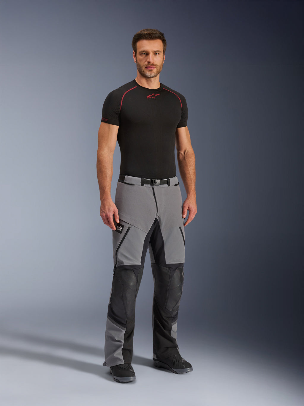 Alpinestars Andes Pro Drystar® XF byxor, äventyrsbyxor för motorcykel, mörkgrå och svarta, bärs av en modell med ett svart tekniskt underställ, med flerpanelskonstruktion, vattentäta dragkedjor och förstärkta zoner för äventyrskörning.