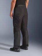 Alpinestars Cusco Drystar® byxor, motorcykelbyxor, svarta, sedda snett bakifrån med lårficka med dragkedja och artikulerade paneler, bärs med svarta motorcykelstövlar, hållbar adventure touring-design med diskret logotyp