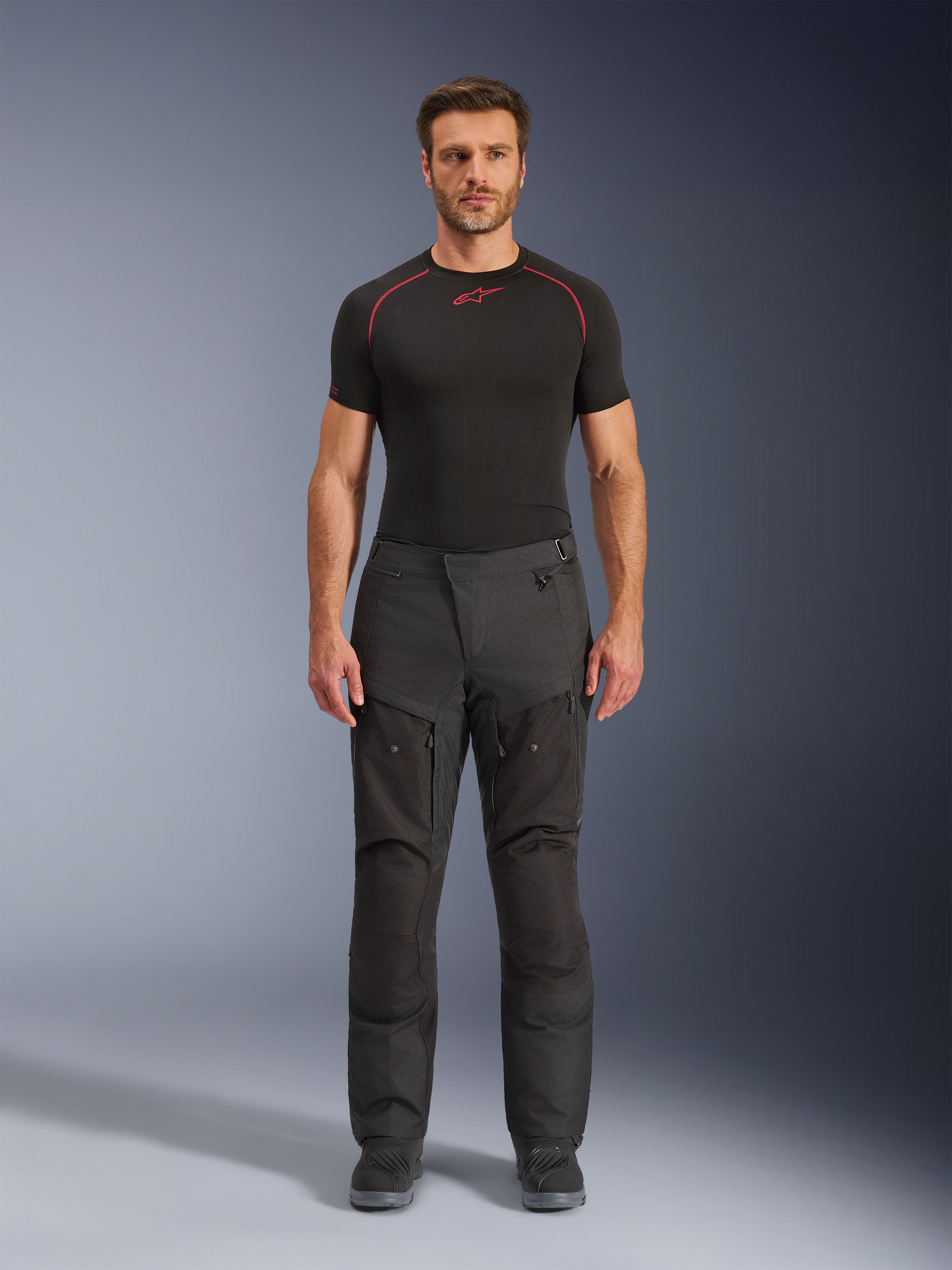 Alpinestars Cusco Drystar® Byxor, MC-byxor i textil, svarta, bärs av en modell med svart underställ och stövlar, adventure touring-design med ventilationspaneler med dragkedja på låren och slitstark konstruktion i flera paneler