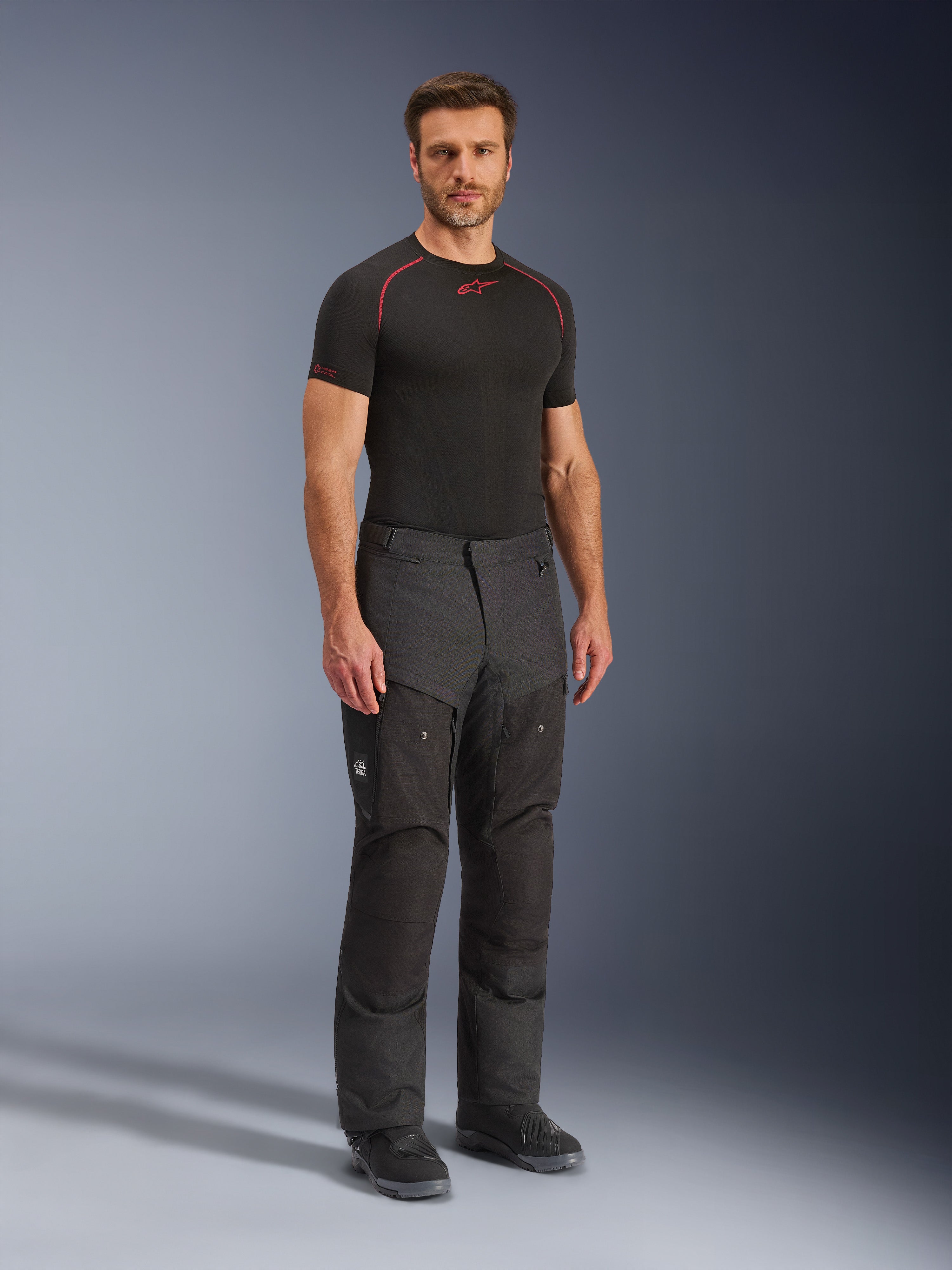 Alpinestars Cusco Drystar® Pants, svarta mc-byxor i textil, bärs av en modell med svart baslager och stövlar, med ripstop-tyg, stora cargofickor med 'Terra'-logotyp och ergonomisk design för äventyrskörning.