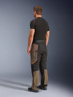 Alpinestars Cusco Drystar® byxor, adventure-motorcykelbyxor, Walnut Black, trekvartsvy bakifrån bärs med ett svart underställ och stövlar, med förstärkta textilpaneler, benfickor med dragkedja på låren och en ergonomisk touring-passform.