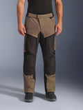 Alpinestars Cusco Drystar® byxor, adventure touring-motorcykelbyxor, valnöt och svart med orange detaljer, framifrån på modell, med teknisk textilkonstruktion, cargofickor och ventilationsdragkedjor, bärs med svarta motorcykelstövlar