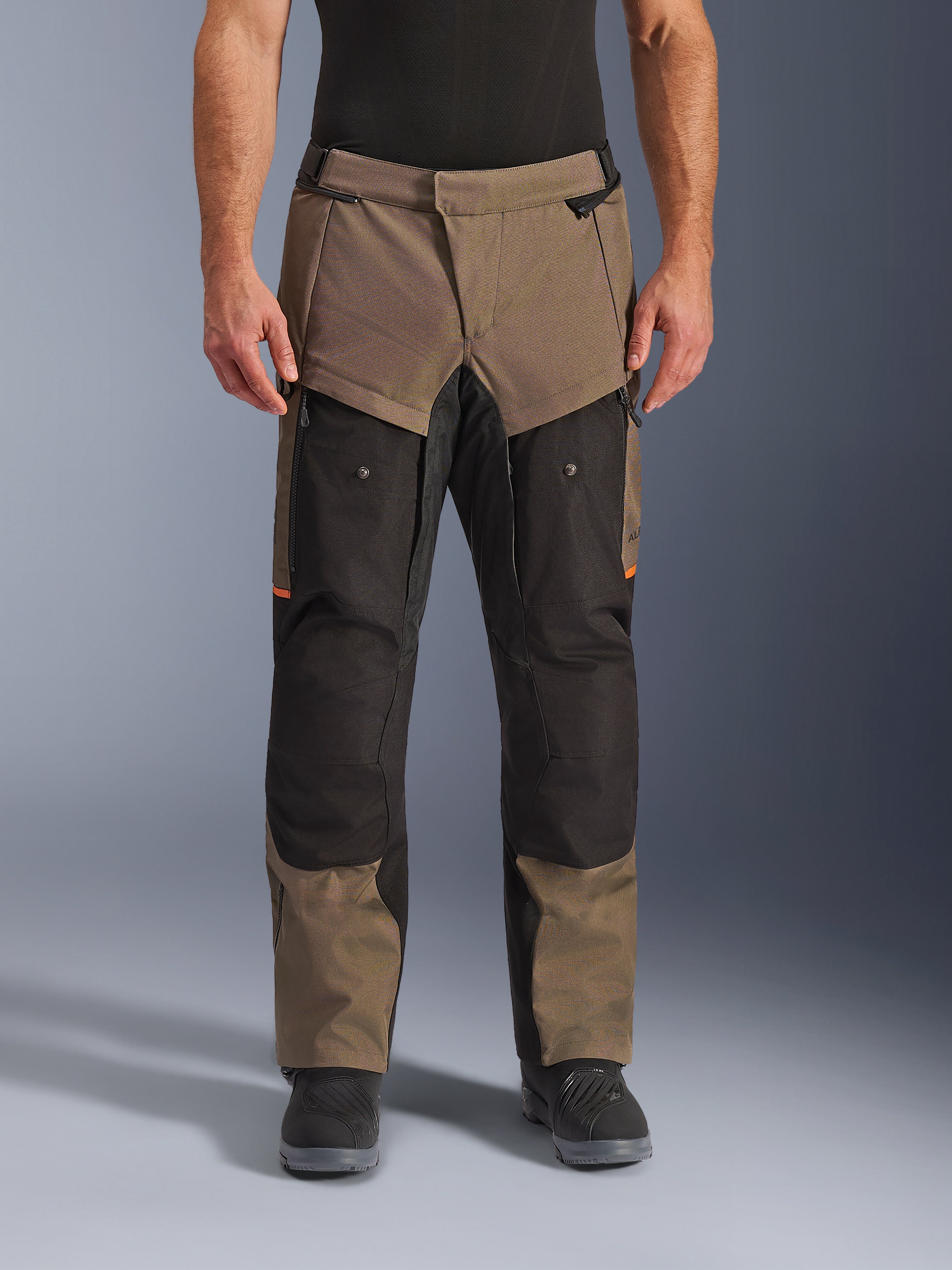 Alpinestars Cusco Drystar® byxor, adventure touring-motorcykelbyxor, valnöt och svart med orange detaljer, framifrån på modell, med teknisk textilkonstruktion, cargofickor och ventilationsdragkedjor, bärs med svarta motorcykelstövlar
