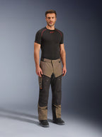 Alpinestars Cusco Drystar® Pants, adventure-motorcykelbyxor, valnöt och svart, bärs av en modell med en svart underställströja och stövlar, med stora benfickor på låren, ventilationsdragkedjor och en robust tvåfärgad design.