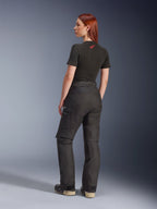 Alpinestars Stella Andes V4 Drystar®-byxor, svarta, äventyrsmotorcykelbyxor som visas från en vinkel snett bakifrån på en modell, kombinerade med en svart t-shirt och stövlar, med cargofickor på sidorna med vit logotyp och hållbar textilkonstruktion.