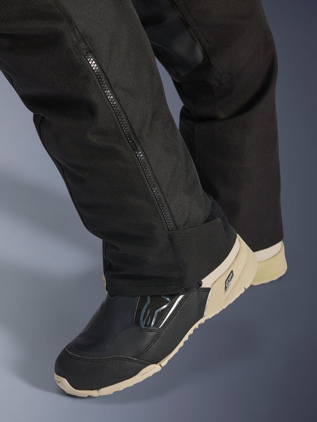 Alpinestars Stella Andes V4 Drystar®-byxor, svarta, närbild på underbenet med en sidodragkedja för justering av stövlar, hållbart textilmaterial, bärs med svarta och beige motorcykelstövlar, äventyrsredo funktionell design
