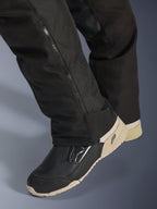 Alpinestars Stella Andes V4 Drystar®-byxor, svarta, närbild på underbenet med en sidodragkedja för justering av stövlar, hållbart textilmaterial, bärs med svarta och beige motorcykelstövlar, äventyrsredo funktionell design