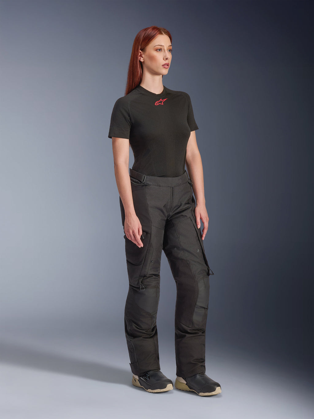 Alpinestars Stella Andes V4 Drystar®-byxor, motorcykelbyxor för dam, svarta, bärs med en svart kortärmad t-shirt med röd logotyp och tekniska skor, adventure touring-design med förstärkta paneler och ventilationsdragkedjor, helbild i trekvartsvy