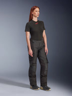 Alpinestars Stella Andes V4 Drystar®-byxor, motorcykelbyxor för dam, svarta, bärs med en svart kortärmad t-shirt med röd logotyp och tekniska skor, adventure touring-design med förstärkta paneler och ventilationsdragkedjor, helbild i trekvartsvy