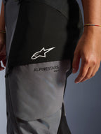 Stella Andes V4 Drystar® dambyxor, svarta och mörkgrå, närbild på övre låret som visar vit stjärnlogotyp och svart Alpinestars-logotyp, hållbart textilmaterial för adventure touring