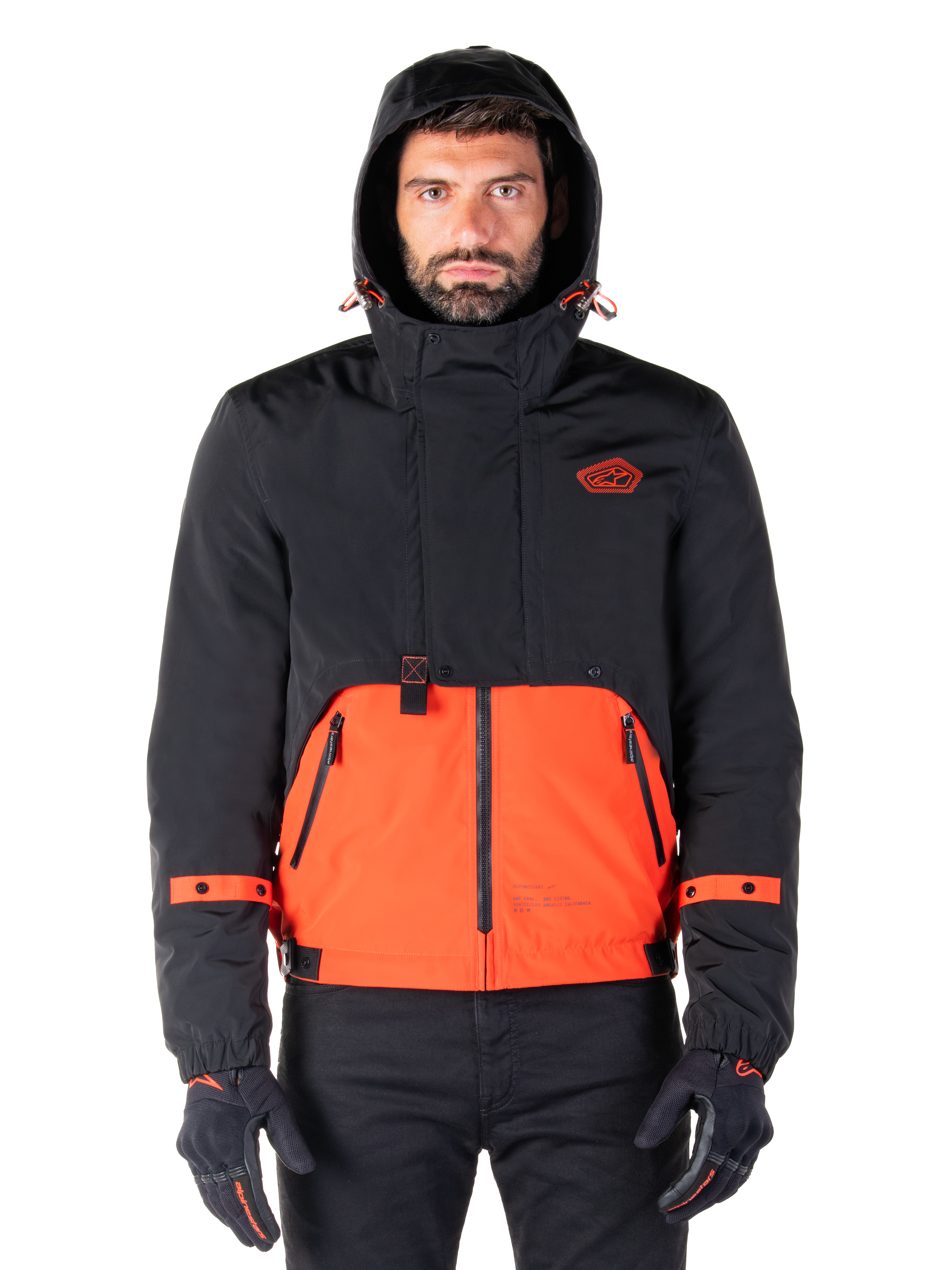 Alpinestars Mootant Waterproof Parka, Motorcycle Jacket, Spicy Orange and Black, modular all-weather design with hood, front zippered pockets, and orange strap details on sleeves, worn by a model with black gloves and pants