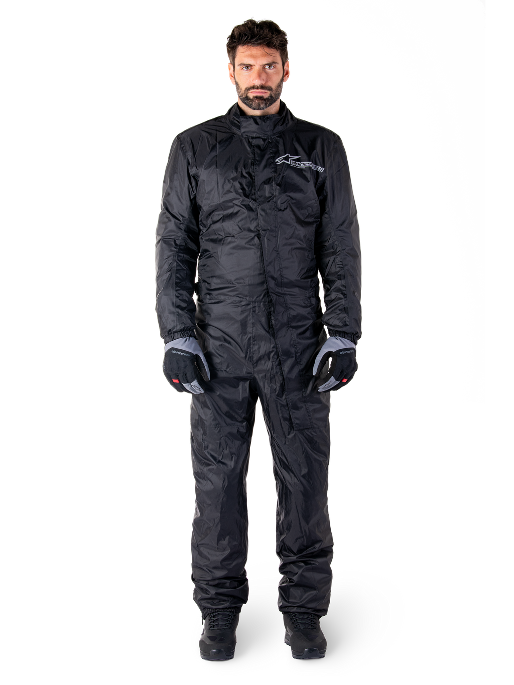Alpinestars Hurricane Rain V2 Suit, helkroppsregnställ för motorcykel i svart, vattentät skyddsutrustning med hög krage och stormstängning fram, vit logotyp på bröstet, bärs med svarta och grå handskar och kängor