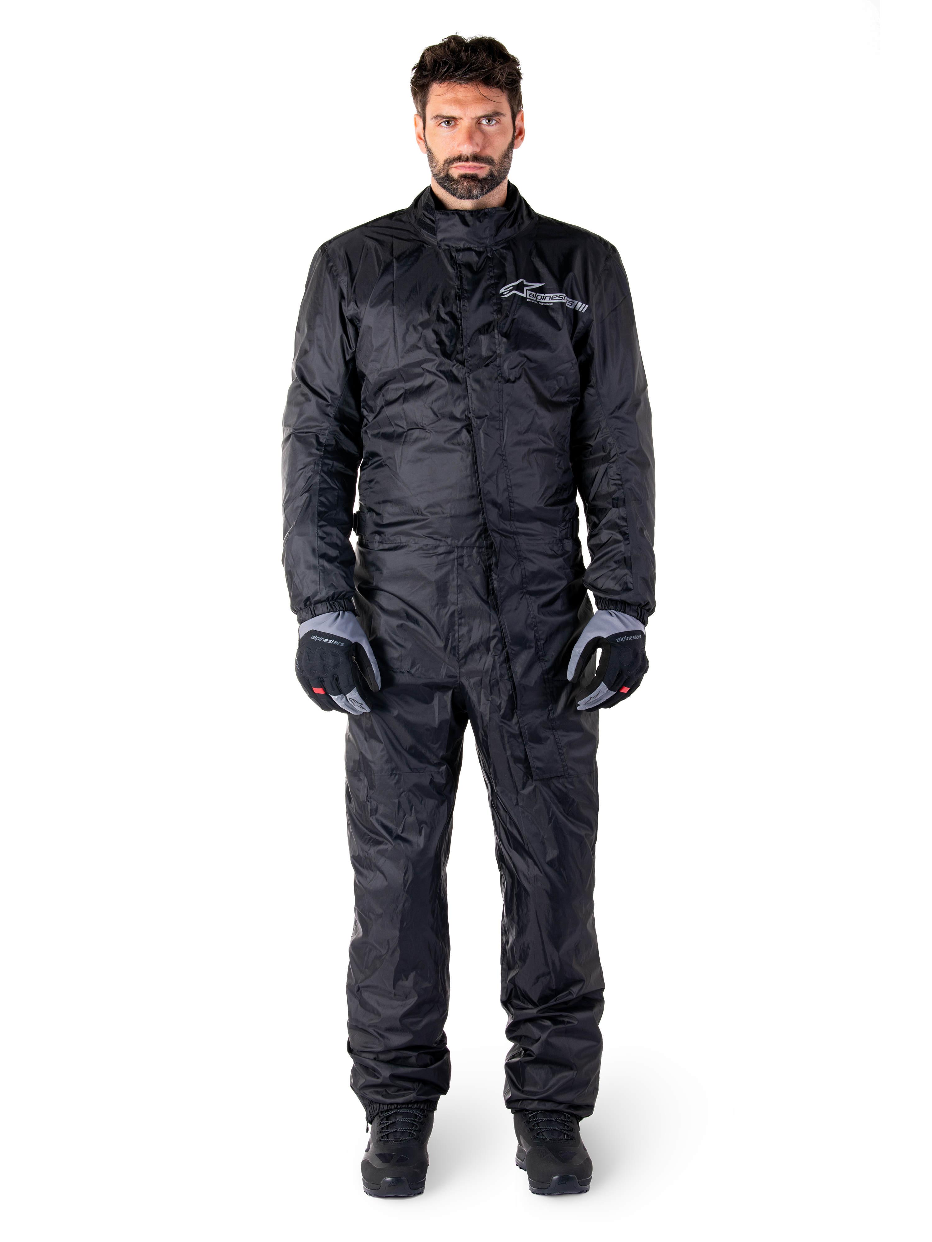 Alpinestars Hurricane Rain V2 Suit, helkroppsregnställ för motorcykel i svart, vattentät skyddsutrustning med hög krage och stormstängning fram, vit logotyp på bröstet, bärs med svarta och grå handskar och kängor