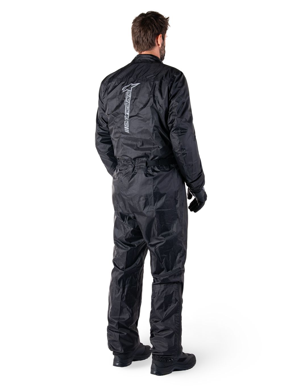 Alpinestars Hurricane Rain V2 Suit, svart vattentätt regnställ för motorcykel i en del, baksida med stor vertikal reflekterande logotyp, lätt vindresistent tyg, bärs med svarta handskar och stövlar