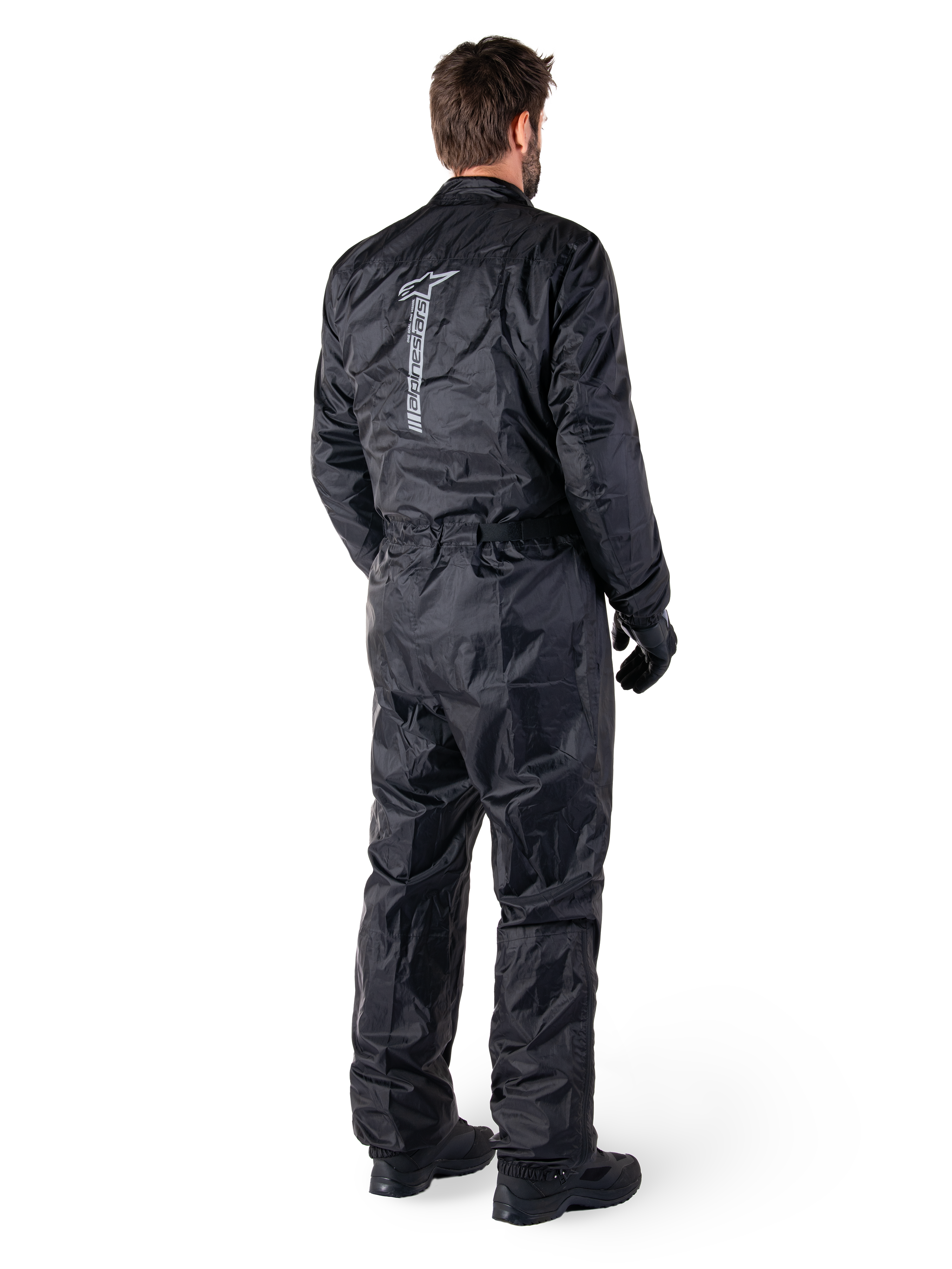 Alpinestars Hurricane Rain V2 Suit, svart vattentätt regnställ för motorcykel i en del, baksida med stor vertikal reflekterande logotyp, lätt vindresistent tyg, bärs med svarta handskar och stövlar