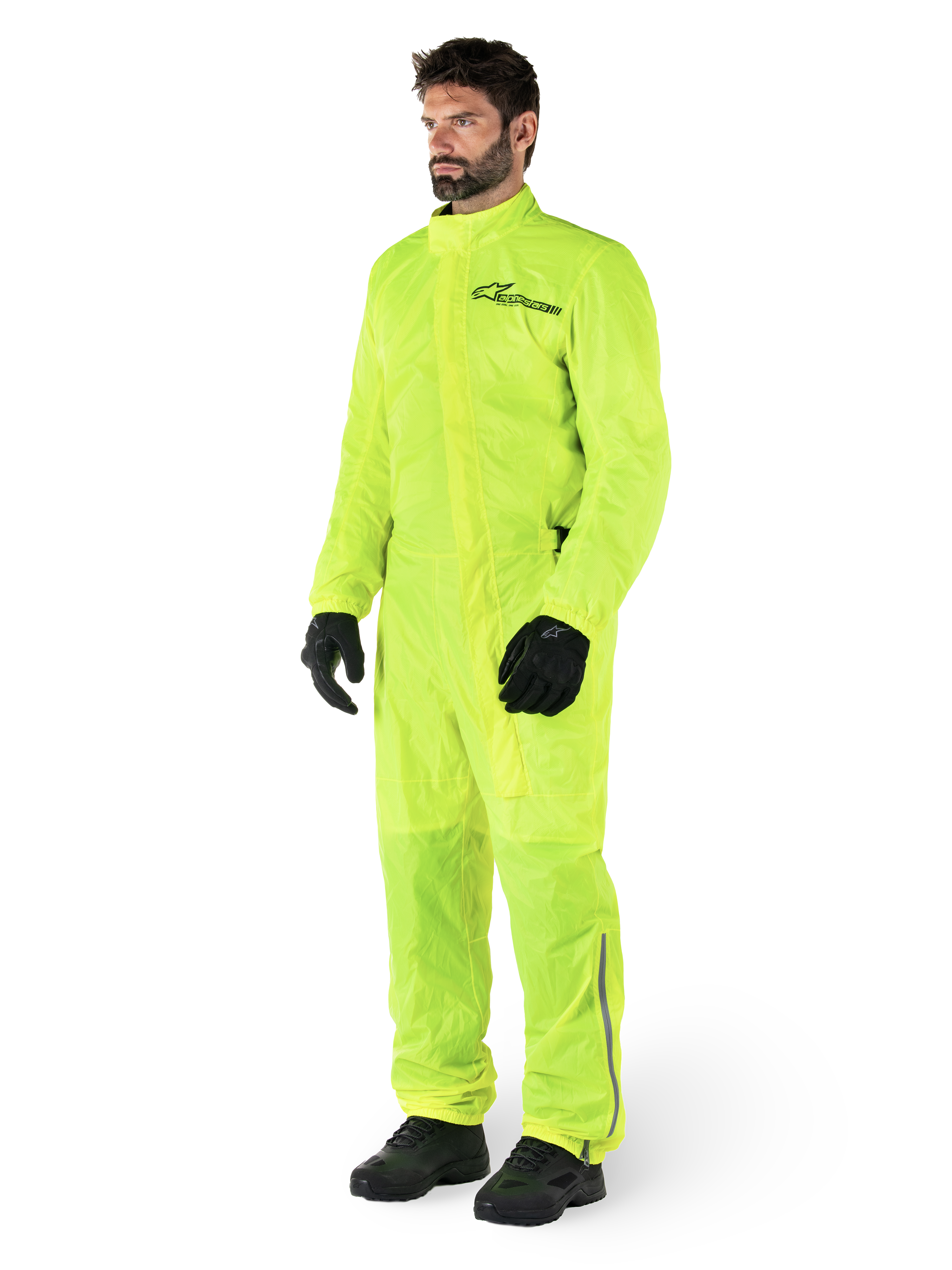 Alpinestars Hurricane Rain V2 Suit, One-piece waterproof motorcycle suit, Yellow Fluo, worn with black gloves and boots, featuring a black Alpinestars logo on the chest and reflective detailing on the legs