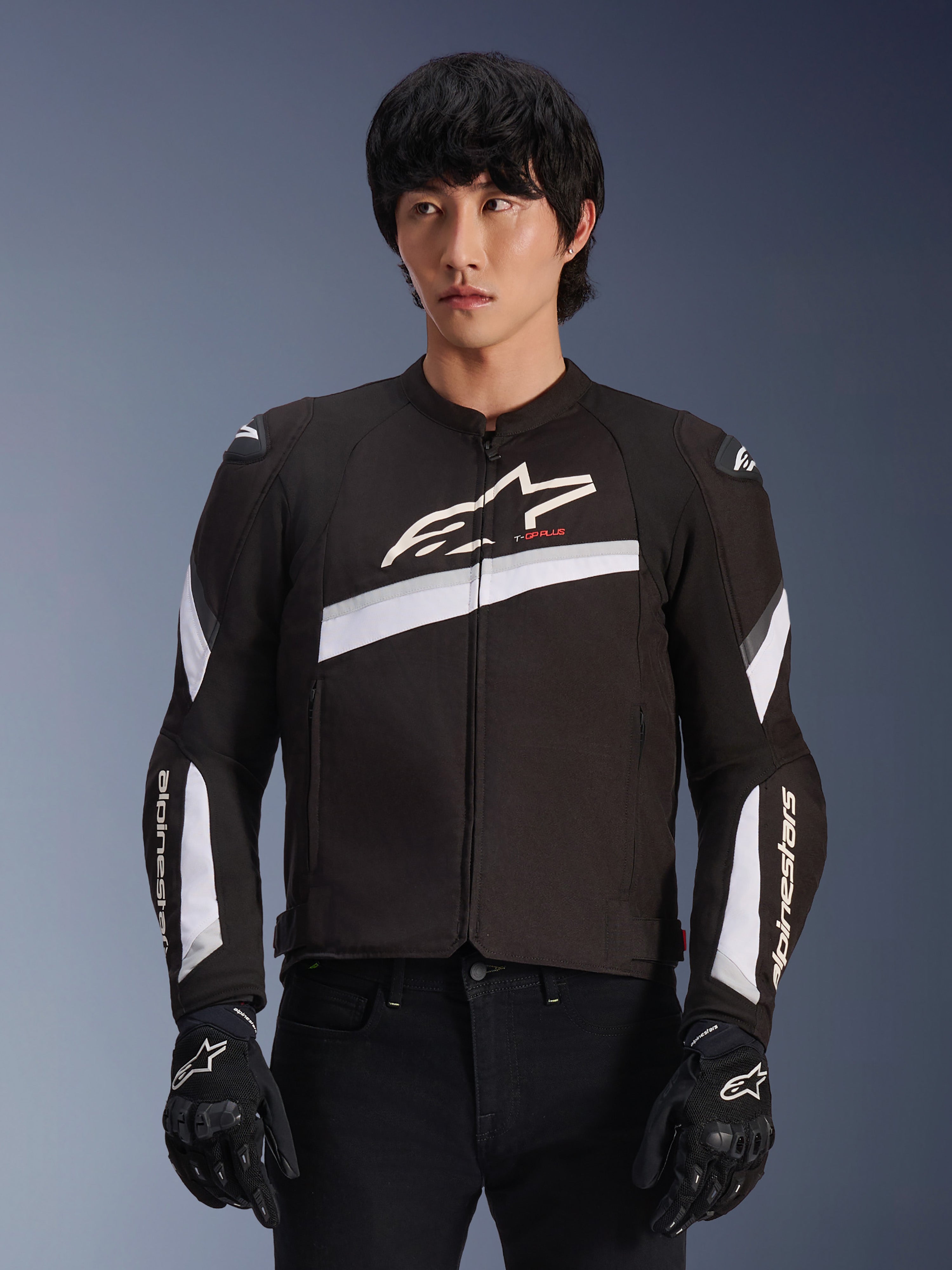 Alpinestars T-GP Plus R V4 Jacket, Black and White, textile motorcycle jacket, featuring white diagonal accents and brand logos on chest and sleeves, worn by a model with black riding gloves, sleek sport-fit design for road riding
