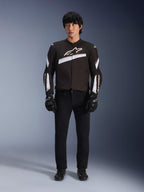 Alpinestars T-GP Plus R V4 Jacket, Black and White, Sport Textile Motorcycle Jacket, worn by a model with black pants and gloves, featuring bold white Alpinestars logo on the chest and sleeves, sleek racing-inspired design