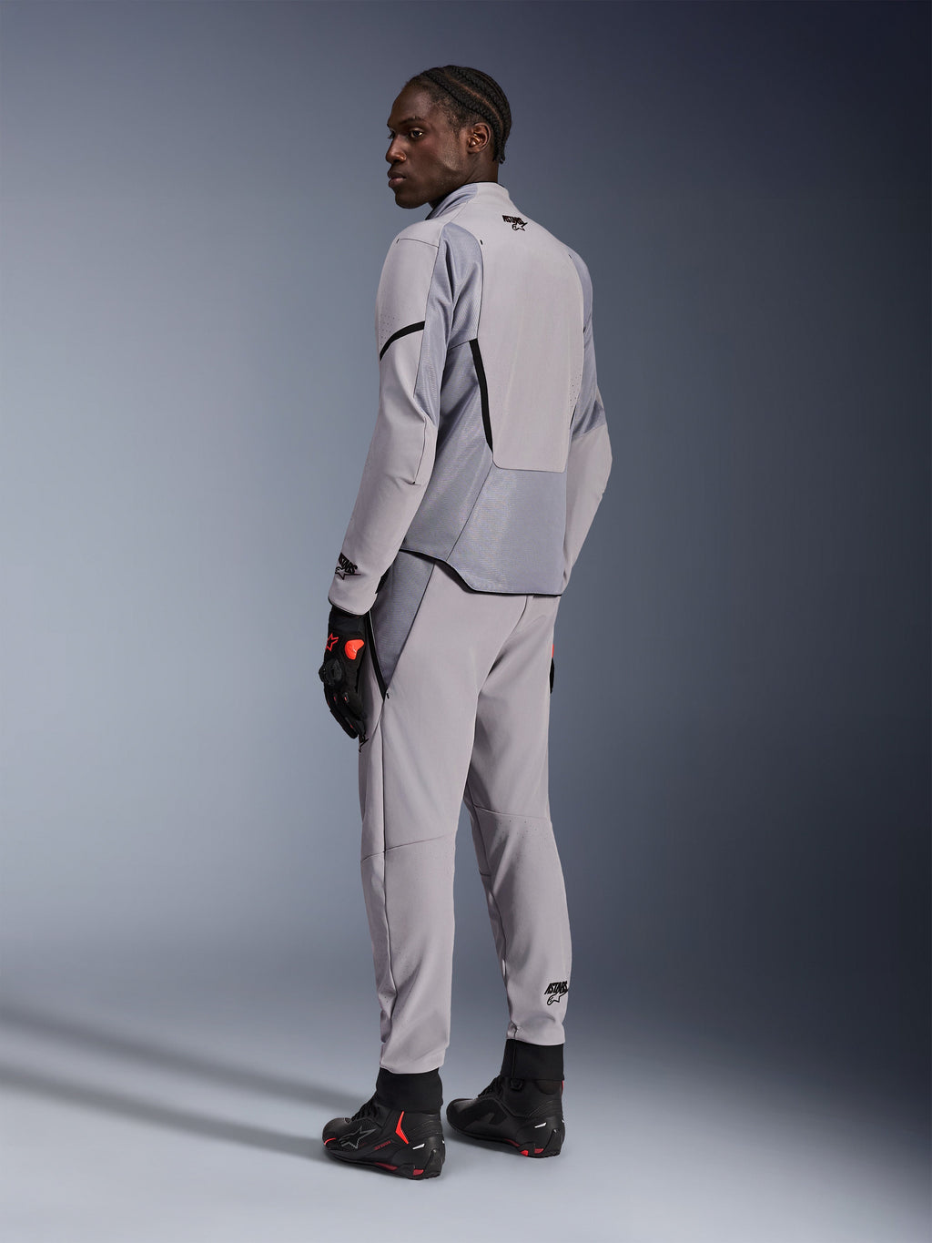 Alpinestars Aeroshell Airflow-jacka i Mid Gray Anthracite, bärs med matchande byxor och svarta racinghandskar, vy bakifrån som visar laserperforerade paneler och atletisk sportpassform, professionell motorcykelutrustning