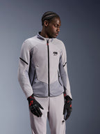 Alpinestars Aeroshell Airflow-jacka, Mid Gray Anthracite, bärs av en modell med matchande textilbyxor och svarta handskar med röda detaljer, med laserperforerade zoner och meshpaneler för ventilation, strömlinjeformad sport-fit-design för motorcykelkörning