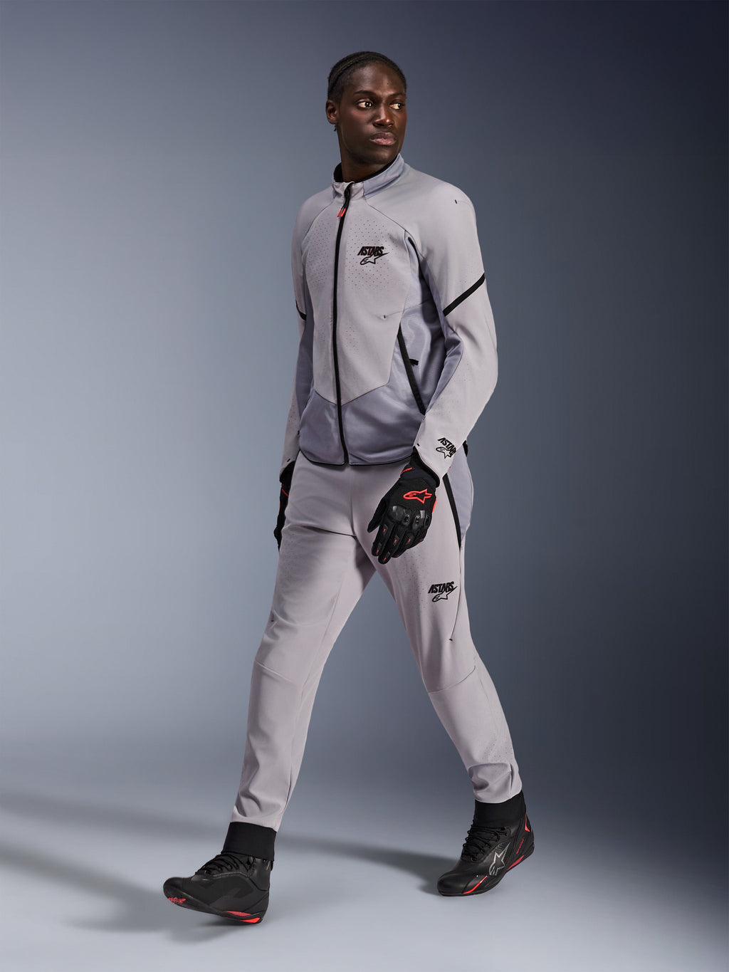 Alpinestars Aeroshell Airflow-jacka i Mid Gray Anthracite, buren av en manlig modell med matchande grå körbyxor och svarta handskar, med laserperforerad ventilation på bröstet och en stilren sportskuren design.
