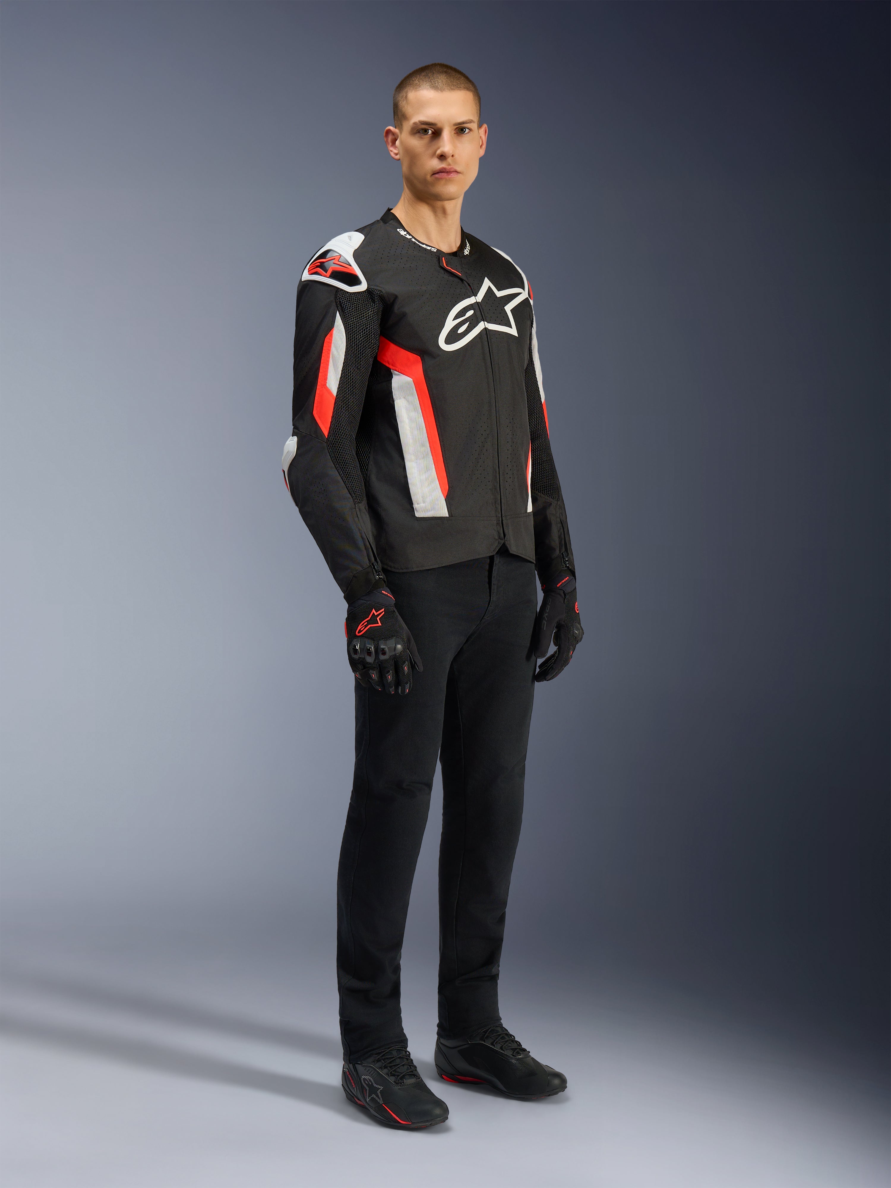 Alpinestars T-GP Air-jacka, Black Red Fluo, bärs av modell med svarta körbyxor och handskar, med laserperforerade textilpaneler, vit Alpinestars-logotyp och röda detaljer, sportig motorcykeljacka för körning på väg i varmt väder