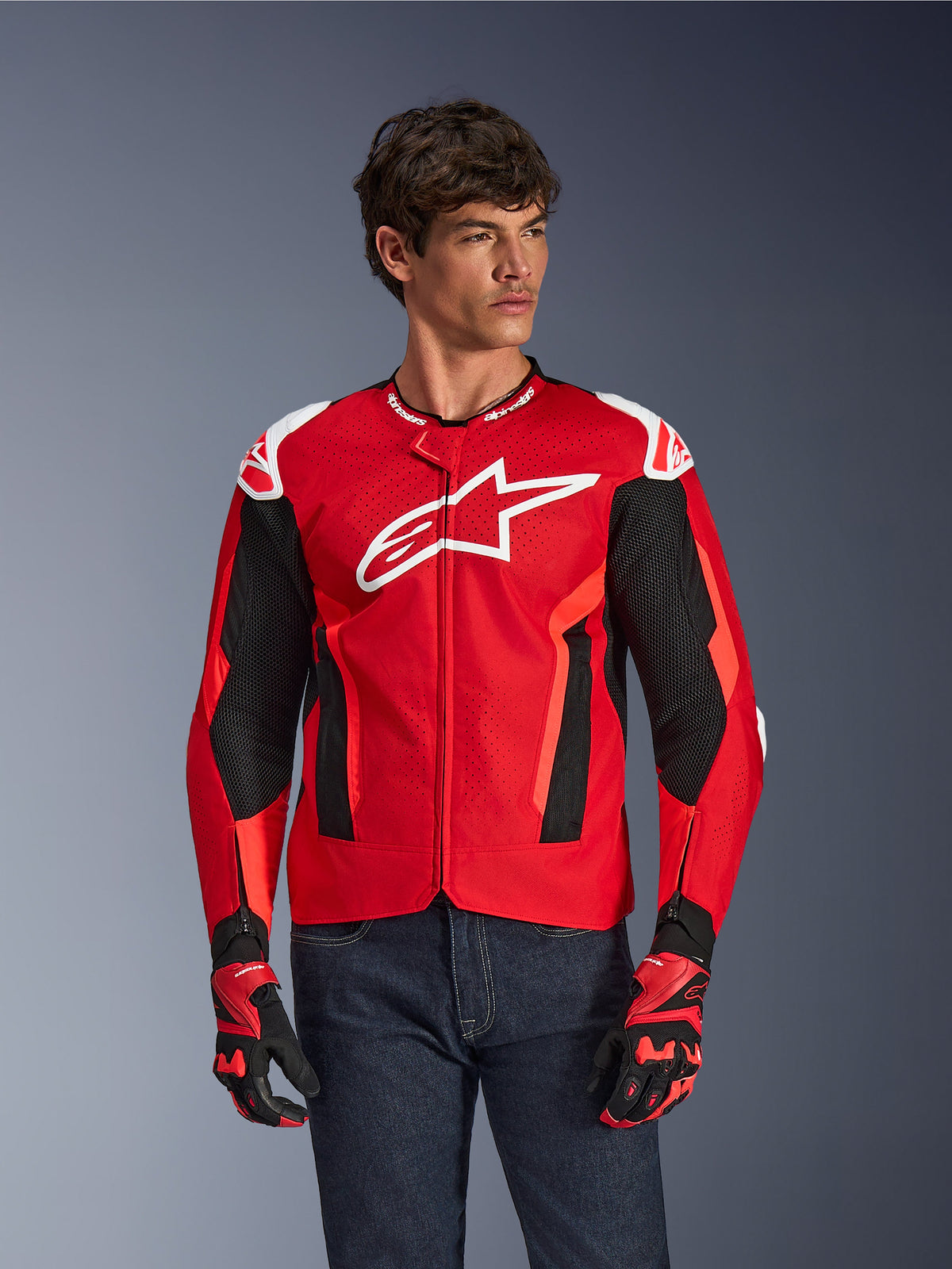 Alpinestars T-GP Air Jacket, motorcykeljacka, klarröd och svart med vit logotyp, med perforerade ventilationspaneler i mesh, buren med matchande handskar och mörka denimjeans, sportig design för körning i varmt väder