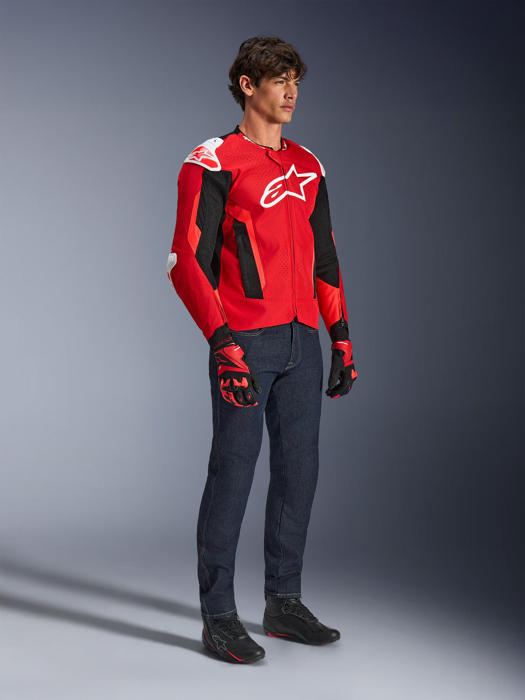 Alpinestars T-GP Air Jacket, Sport Motorcycle Jacket, Bright Red and Black with white accents, worn by a model with dark blue jeans and red racing gloves, featuring high-flow mesh panels and white shoulder sliders, aerodynamic sport fit for warm weather riding.