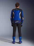 Alpinestars T-GP Air Jacket, Bright Blue Navy White, back view showing aerodynamic hump and mesh ventilation panels, white Alpinestars logo on lower back, worn with black pants and blue racing boots